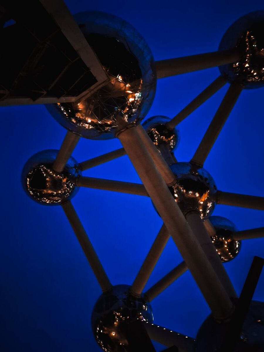 Een close-up van de zilverkleurige bollen en buizen van het Atomium, gefotografeerd tegen een diepblauwe avondlucht. De bollen reflecteren lichtjes van de omgeving.