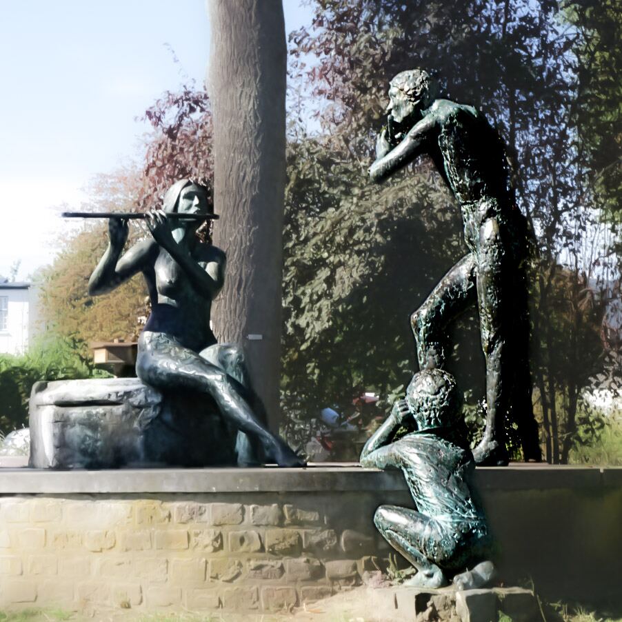 Een bronzen beeldengroep van drie figuren in een parkachtige omgeving. Een zittende vrouw speelt fluit, een staande man luistert en een hurkend kind kijkt toe. Op de achtergrond zijn bomen en een gebouw zichtbaar.