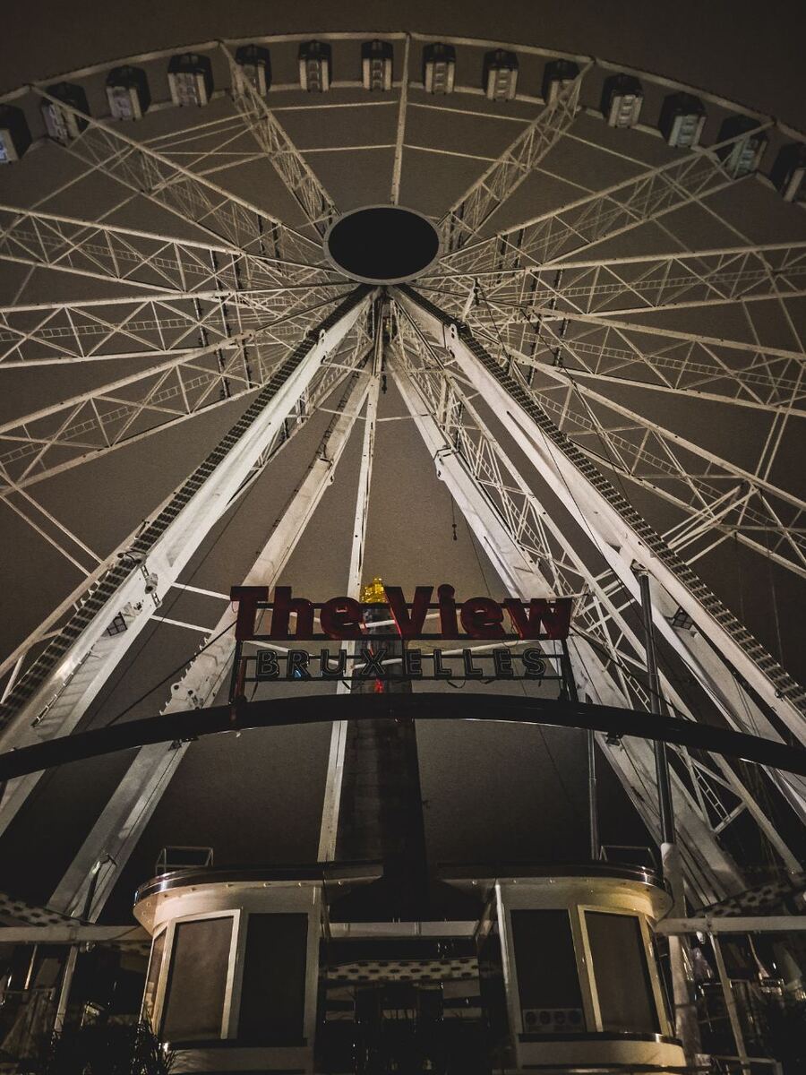 Een nachtfoto van een groot reuzenrad met de tekst 'The View Bruxelles' in rode letters op de voorgrond. De gondels zijn zichtbaar en het rad is verlicht.