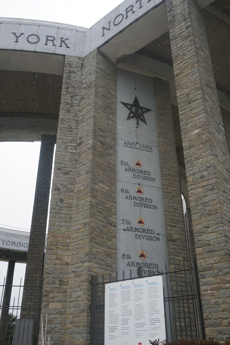 Een close-up van een stenen monument met de tekst 'YORK' en 'NORTH' bovenaan, en een lijst van 'ARMY UNITS' met 'ARMORED DIVISION' eronder. Er is een metalen ster met een bladmotief zichtbaar en een informatiebord in meerdere talen over renovatie.